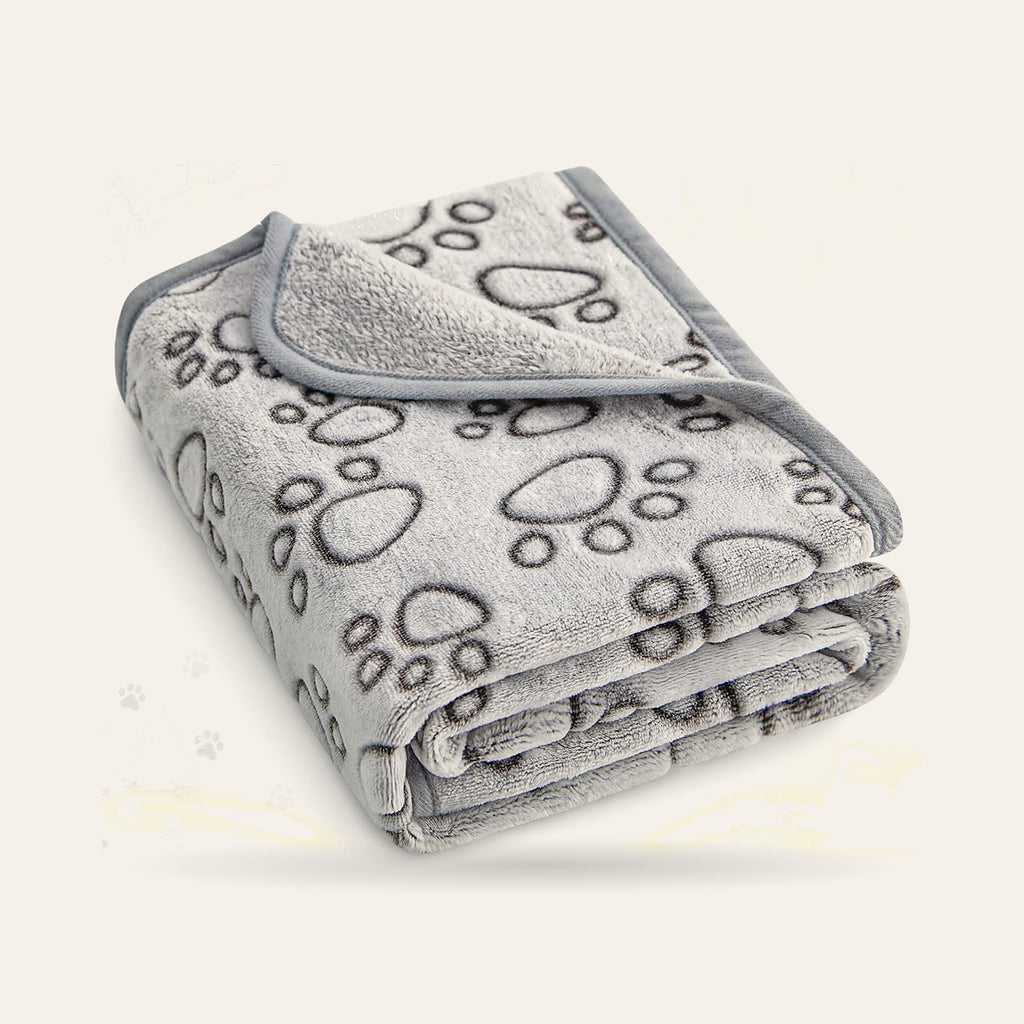 Couverture grise en polaire à motif de pattes, pliée, sur fond ivoire