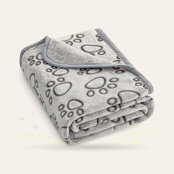 Couverture grise en polaire à motif de pattes, pliée, sur fond ivoire